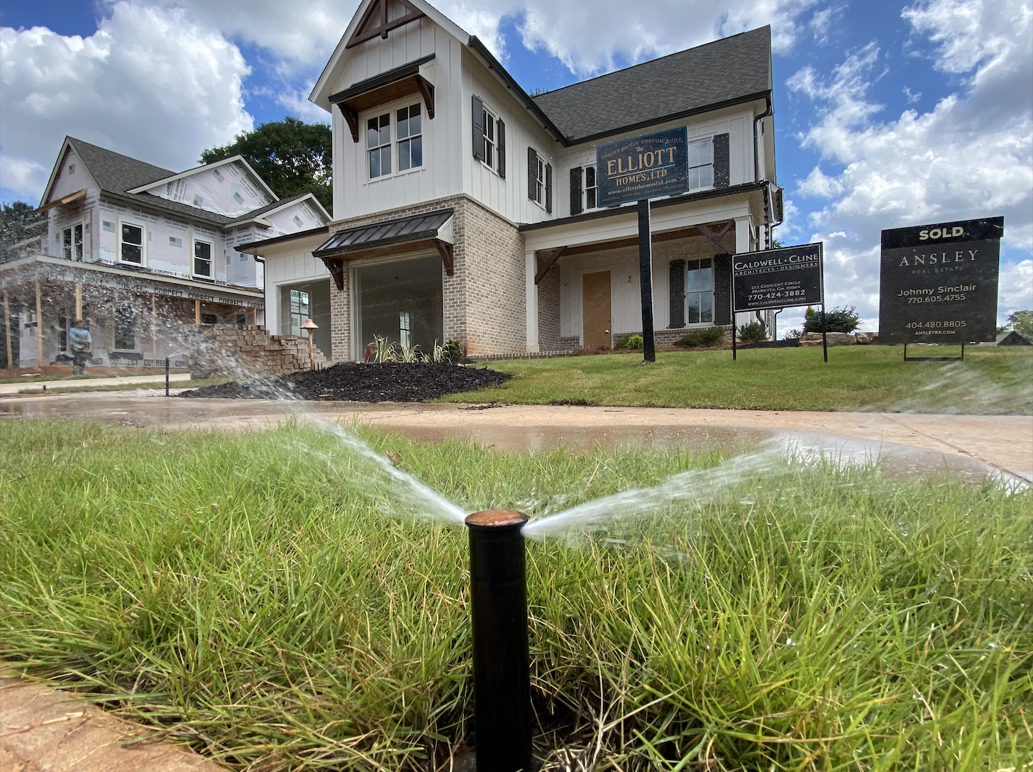 A sprinkler spraying water on a lawn in front of a house, creating a refreshing and vibrant scene.